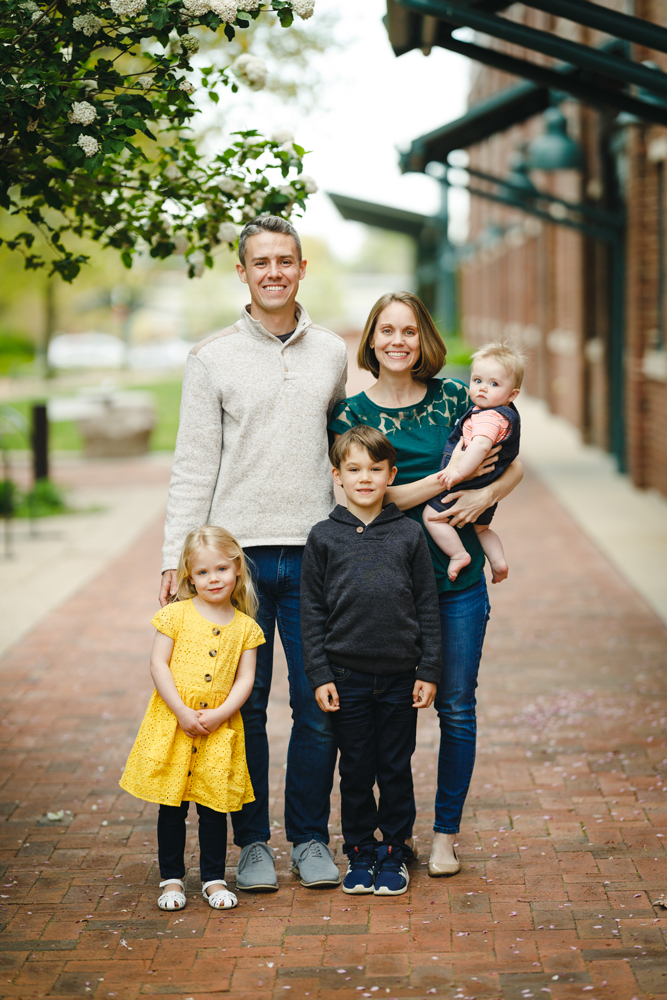 matt, his wife, and their three young children stand on a brick sidewalk next to a tree while smiling